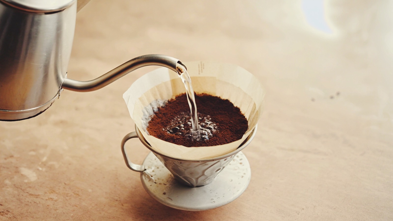 Aus einem schmalen Schwanenhals-Kessel läuft ein dünner Wasserstrahl kreisend über ein Kaffeebett im Papierfilter.